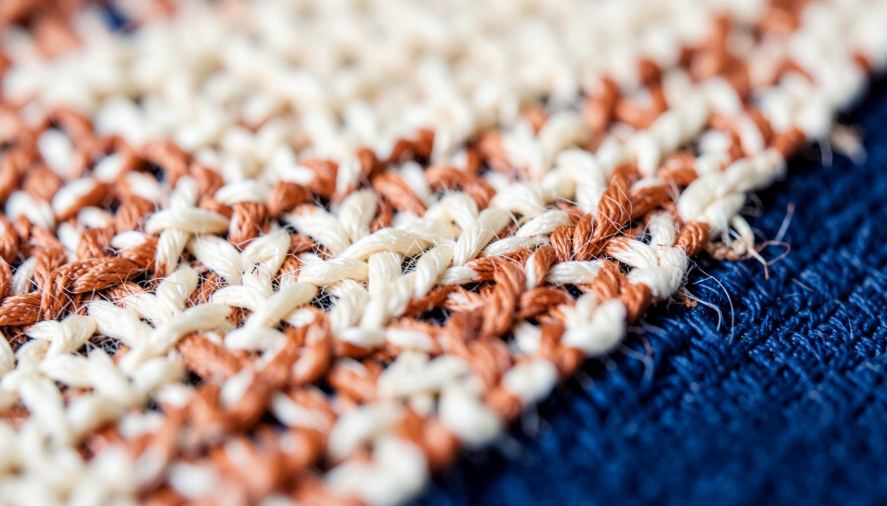 Extreme close-up of woven textile threads in soft cream and rust tones, warm and tactile