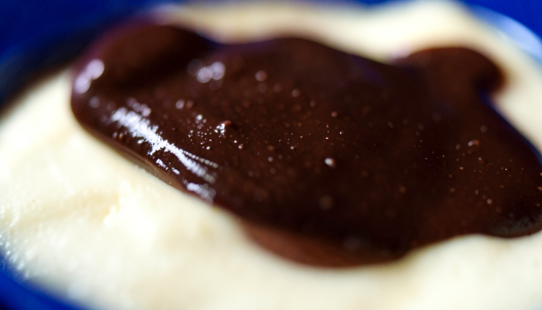 Extreme close-up of rich brown chocolate drizzle on a cream surface, glossy and inviting