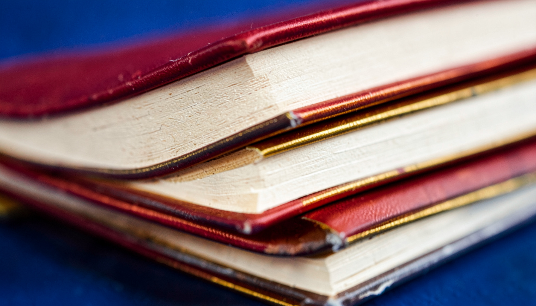 Extreme close-up of stacked book spines in warm reds, creams, and ochres with gold foil edges