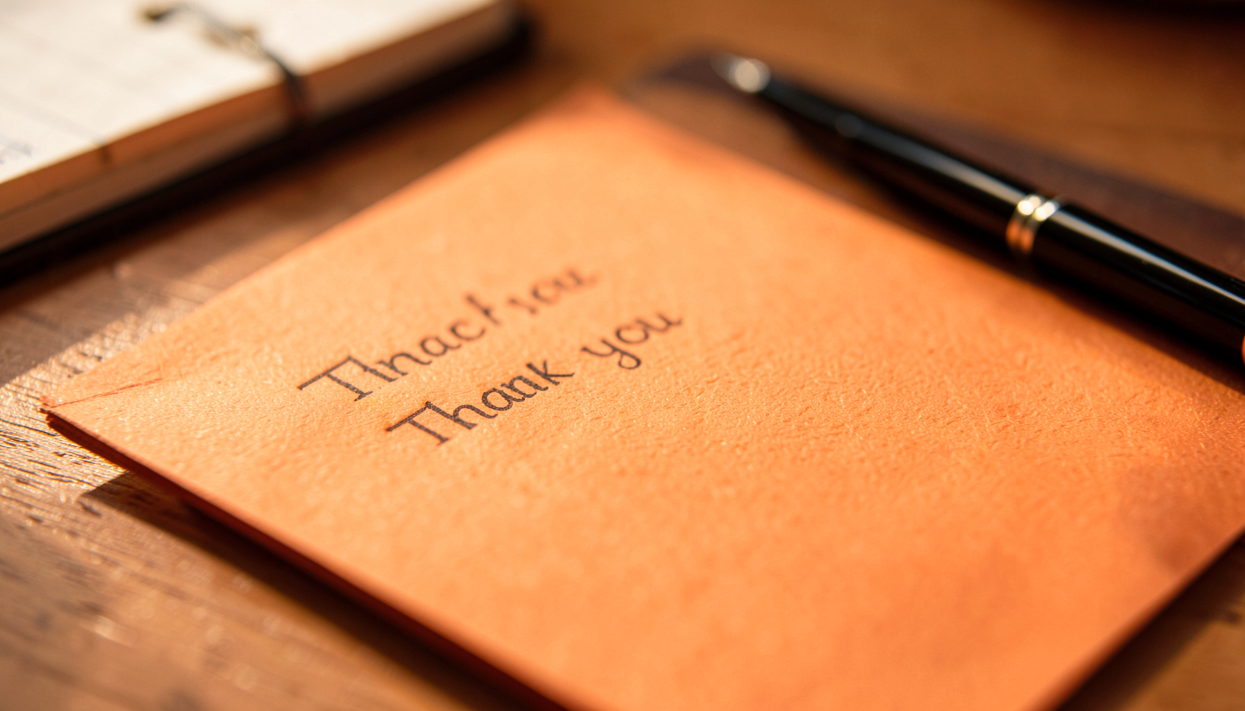 A thank-you note on a desk beside a notebook and pen, warm morning light